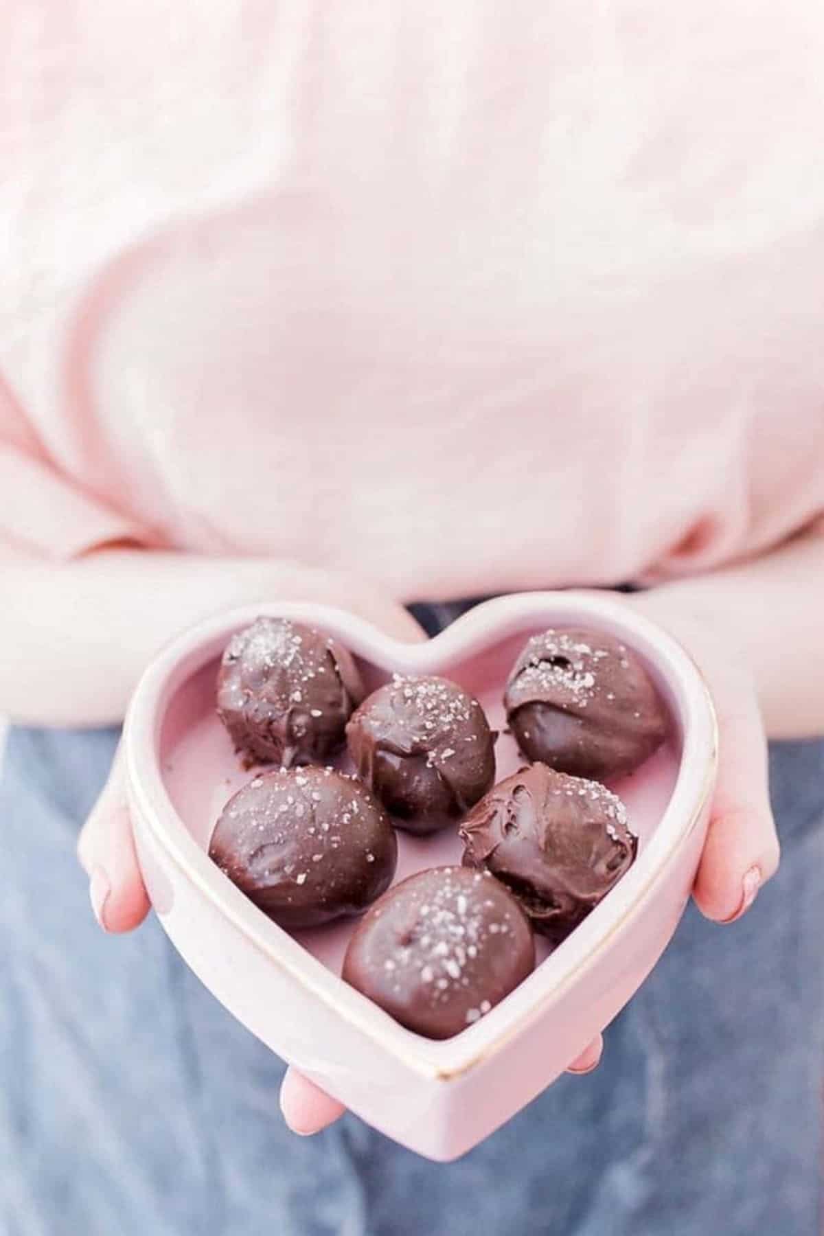 salted dark chocolate truffles in a heart shaped box being held by a woman