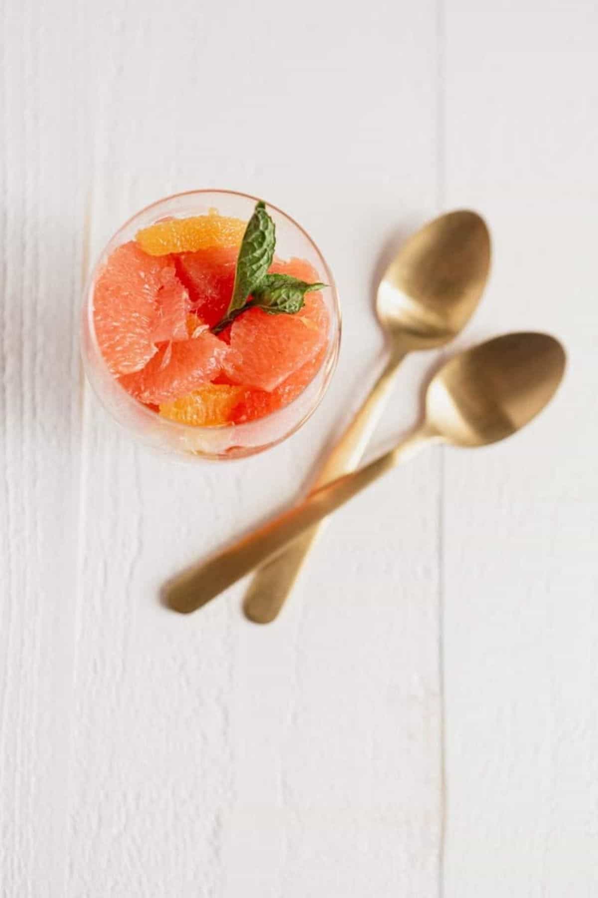 one citrus fruit cup with two gold spoons