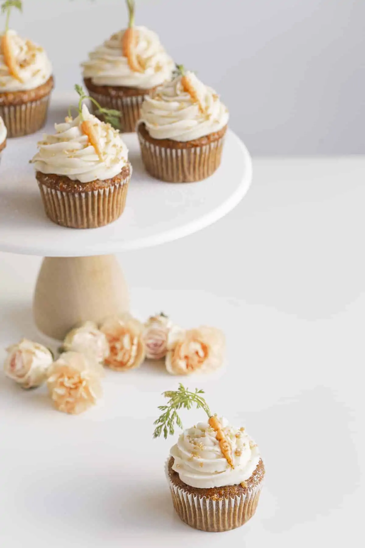 small batch carrot cupcakes on a stand with flowers and carrots