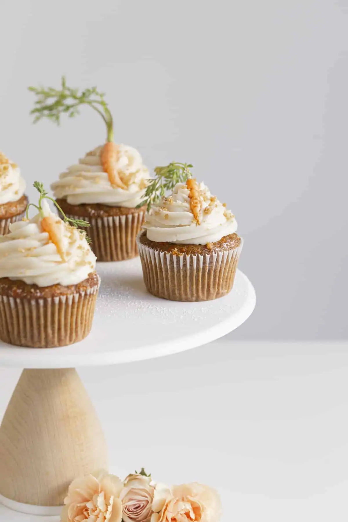 spiced carrot cupcakes on a cake stand with mini carrots and flowers