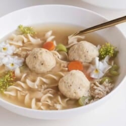 matzo ball soup in a bowl with noodles, chicken, veggies, and edible flowers