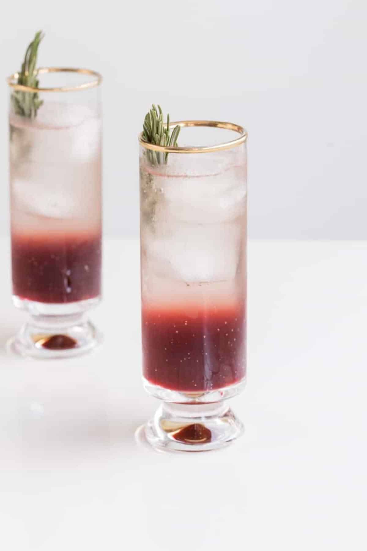 2 glasses with layered cocktail, ice, and rosemary