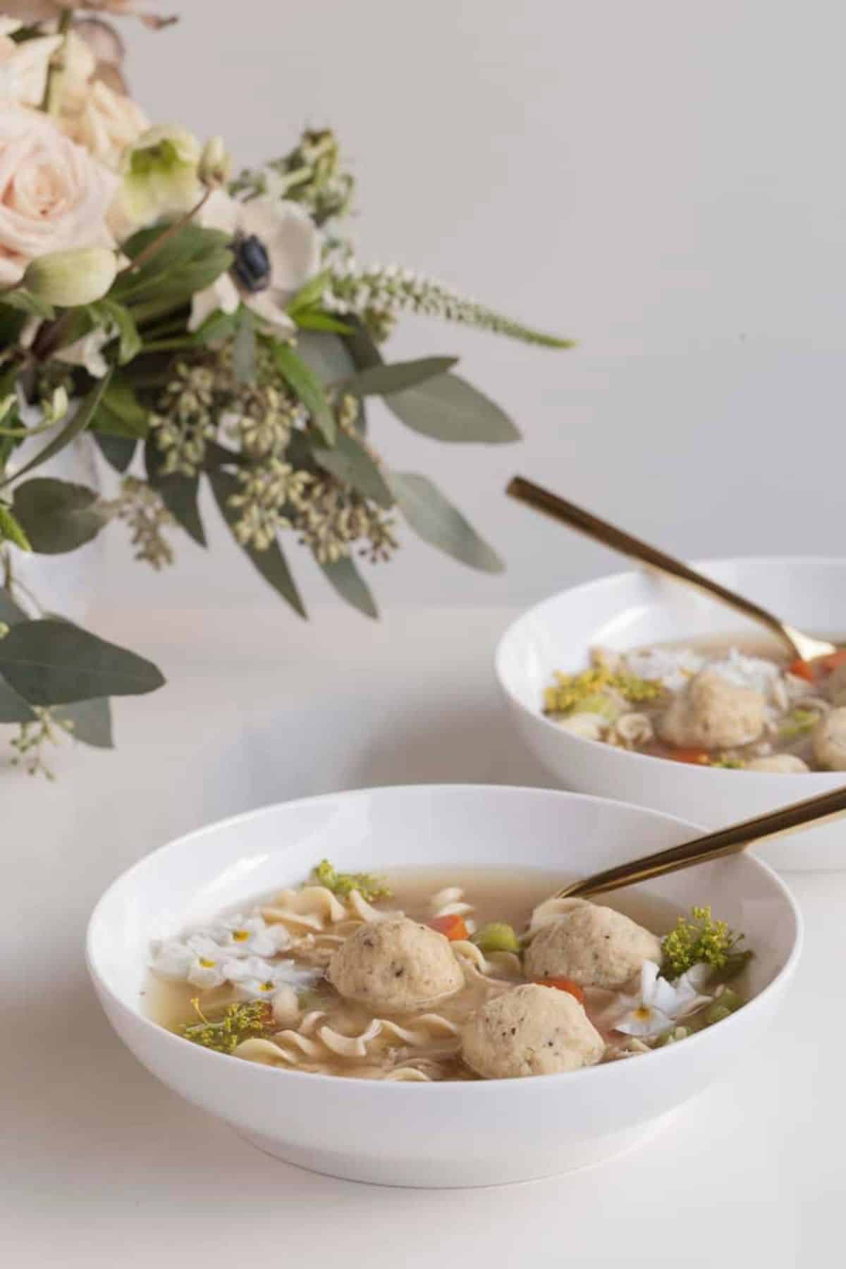 matzo ball soup on a table in two bowls with flower arrangment