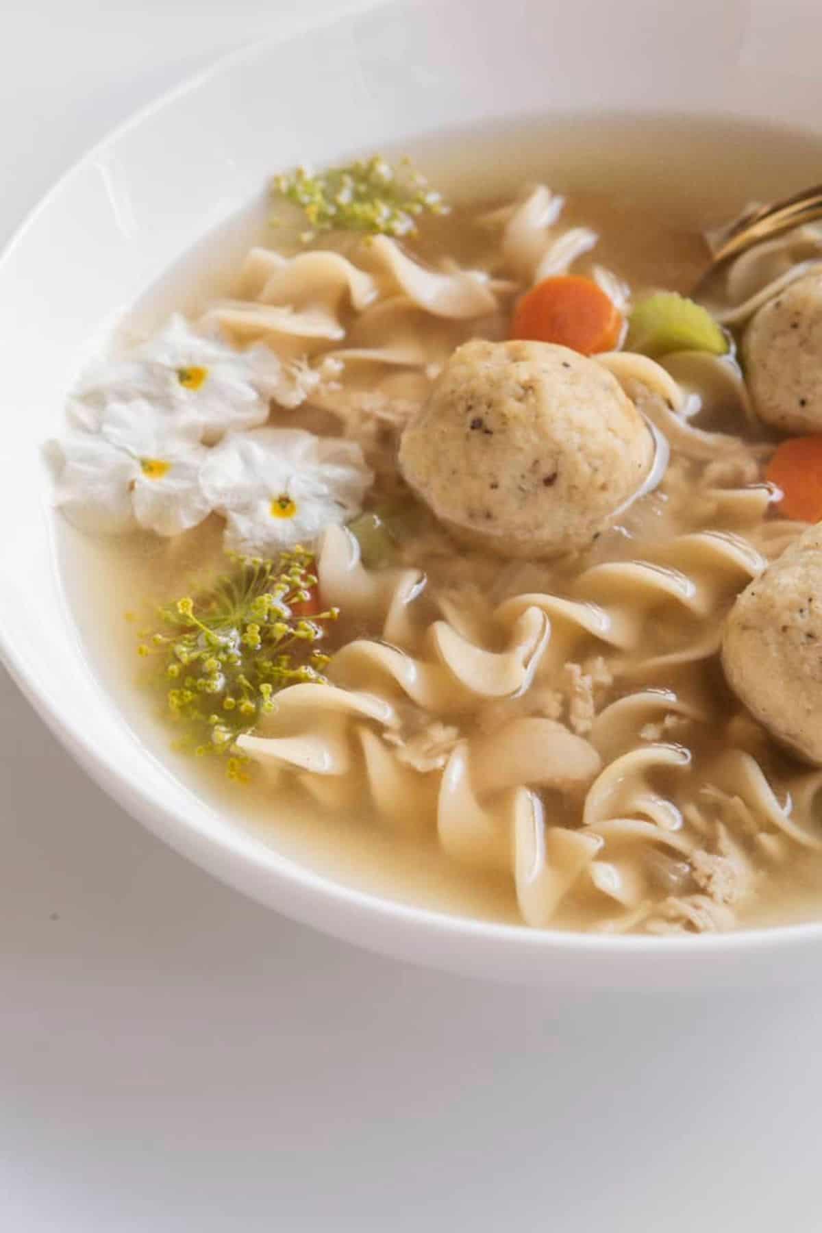 soup in a bowl with noodles, chicken, veggies, and edible flowers