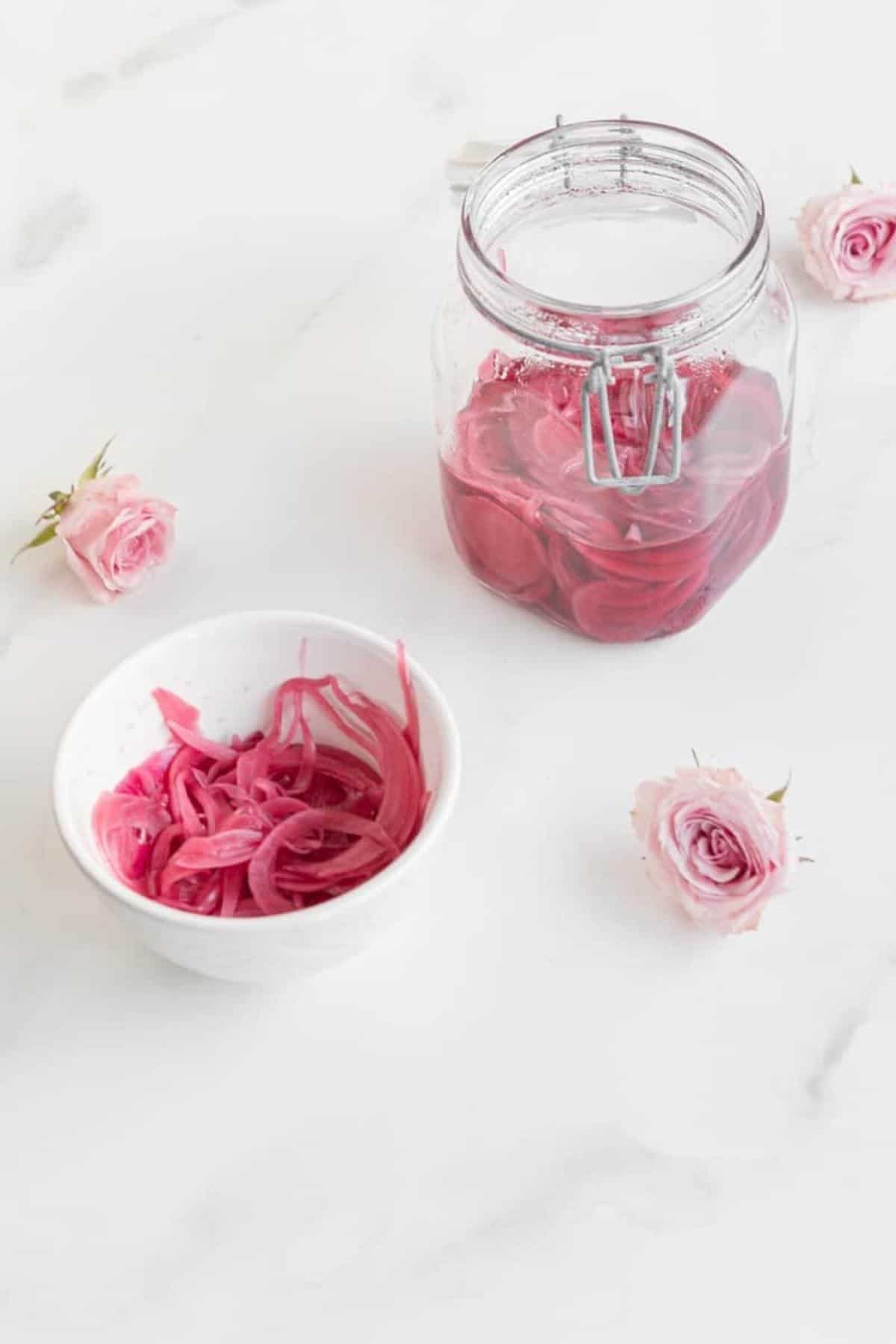 quick pickled onions in a jar and in a bowl with flowers and marble