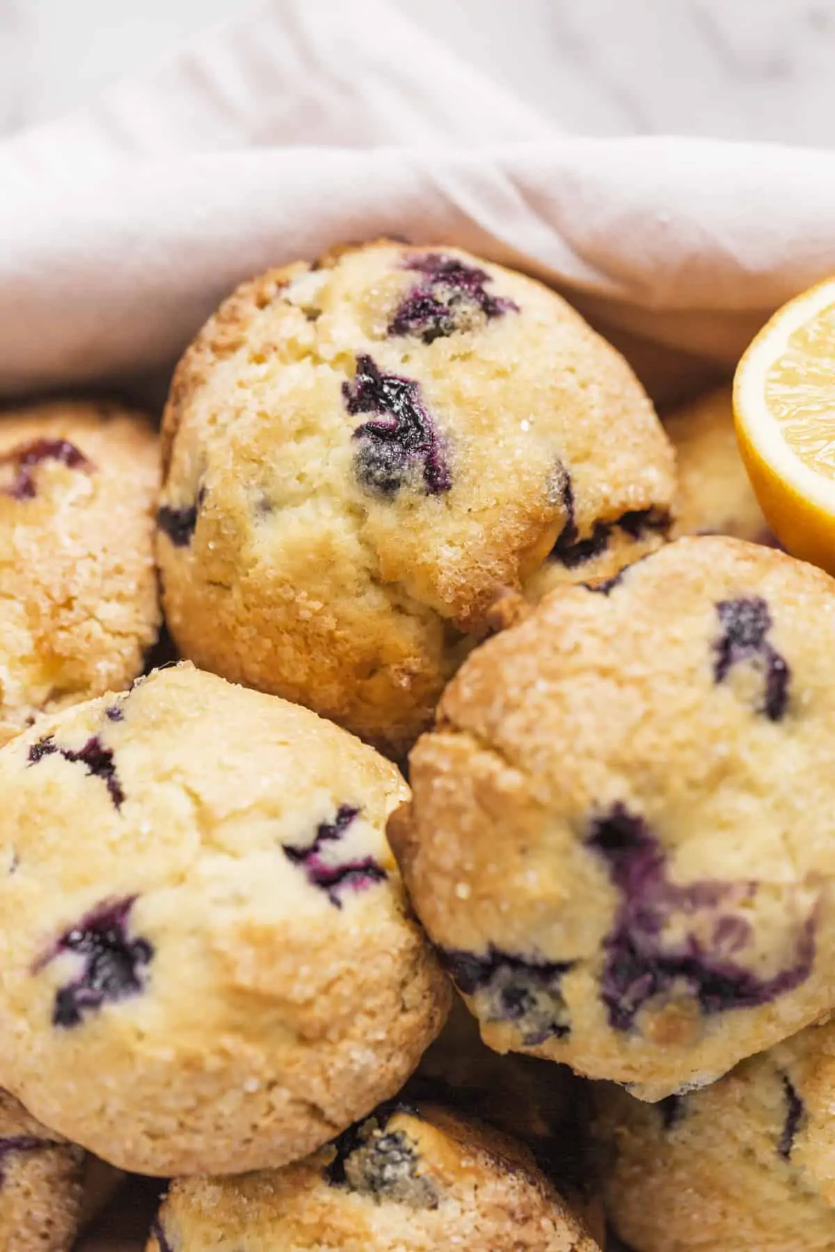 bakery style blueberry muffins in a basket with a linen and lemon