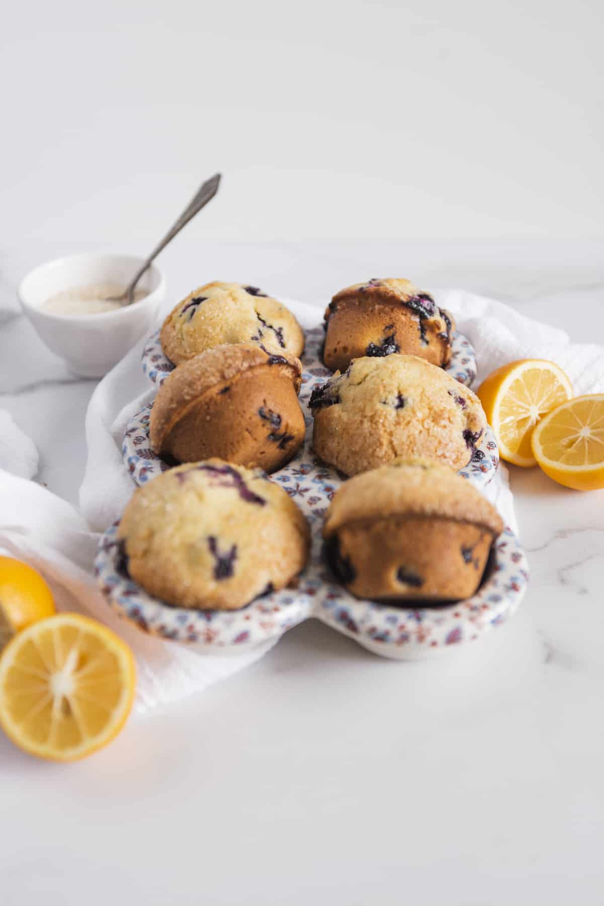 homemade muffins in a ceramic baker with lemon halves and a bowl of sugar