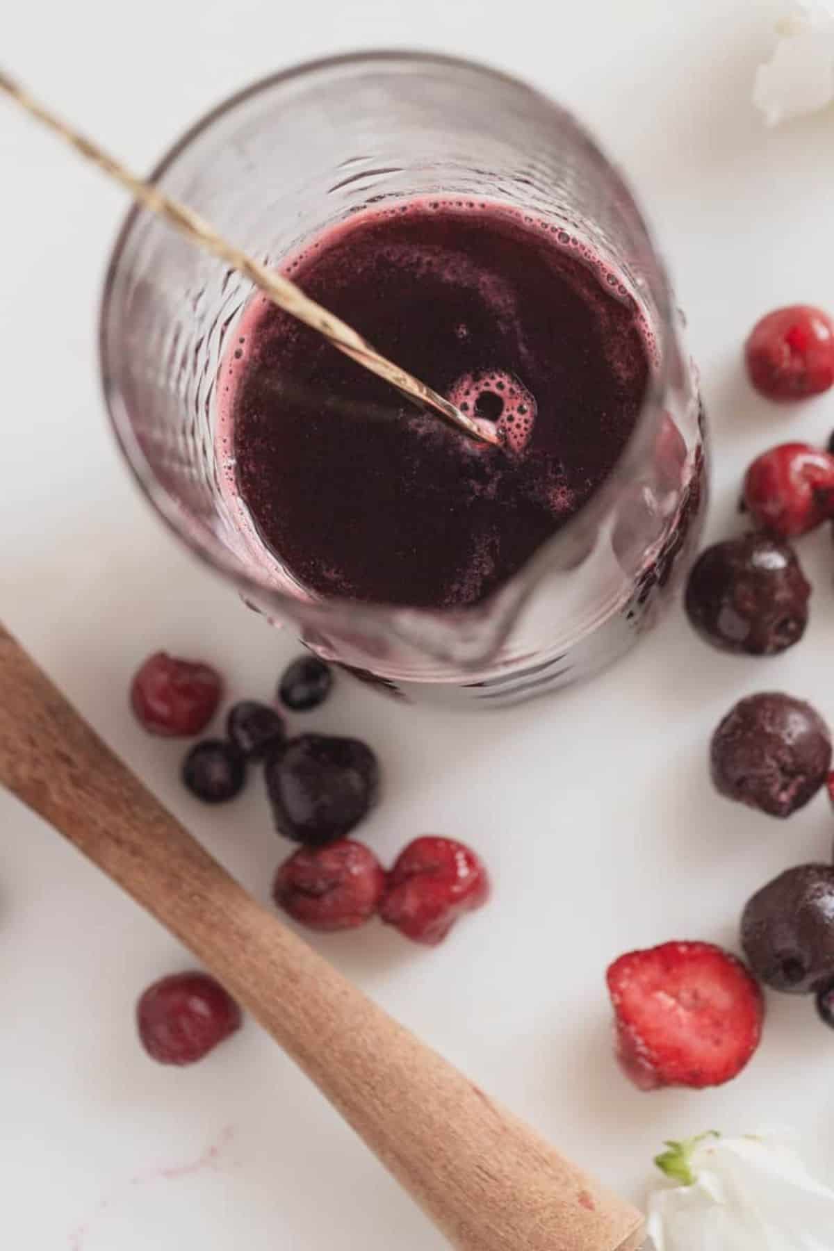 berry simple syrup in a glass pitcher with fruit on counter