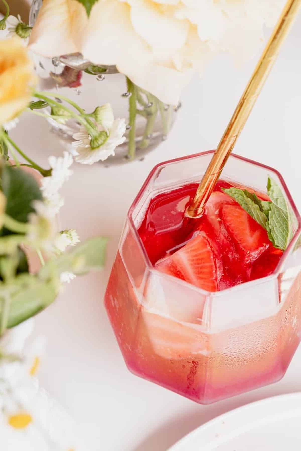 rose berry sangria in a glass with a gold straw and flowers