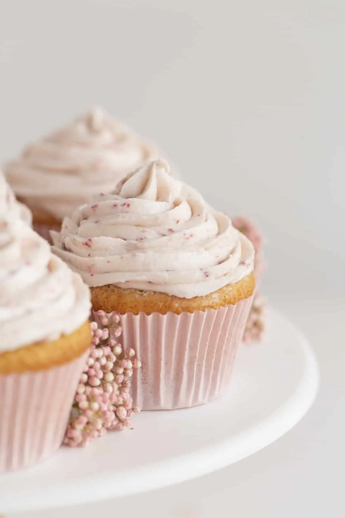 strawberry jam filled cupcakes on a cake stand with icing and flowers