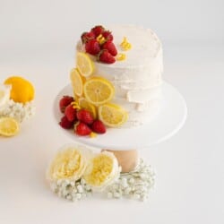 strawberry lemon cake on a white cake stand with lemons and strawberries