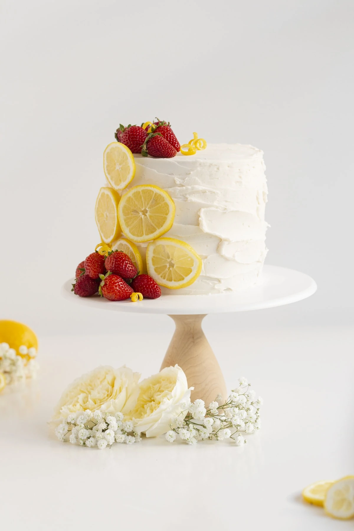 cake with strawberry filling on a cake stand with strawberries, lemons, and flowers