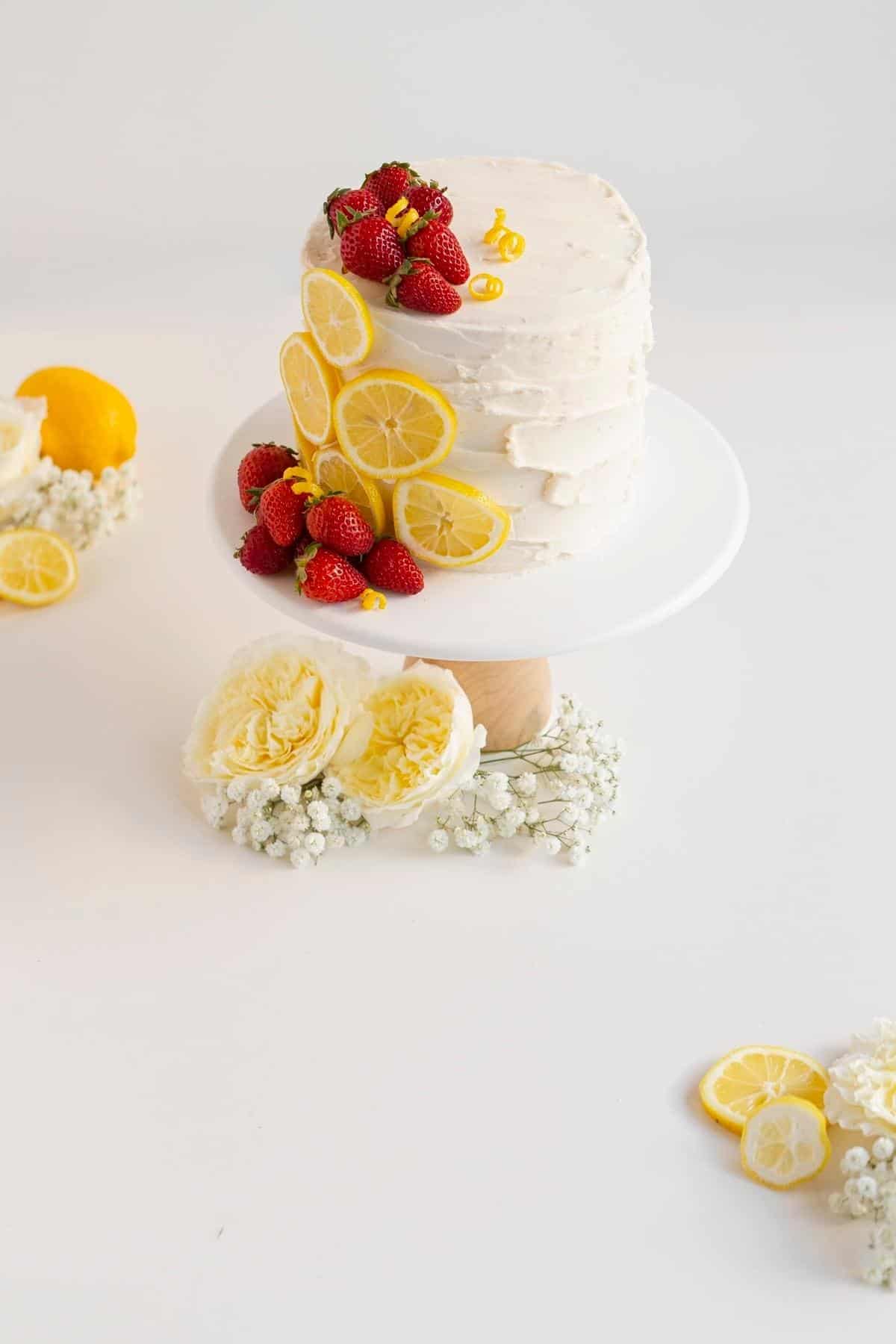 strawberry lemon cake on a white cake stand with lemons and strawberries