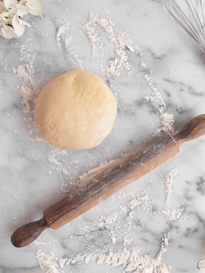 pie dough on a marble surface with flour and rolling pin