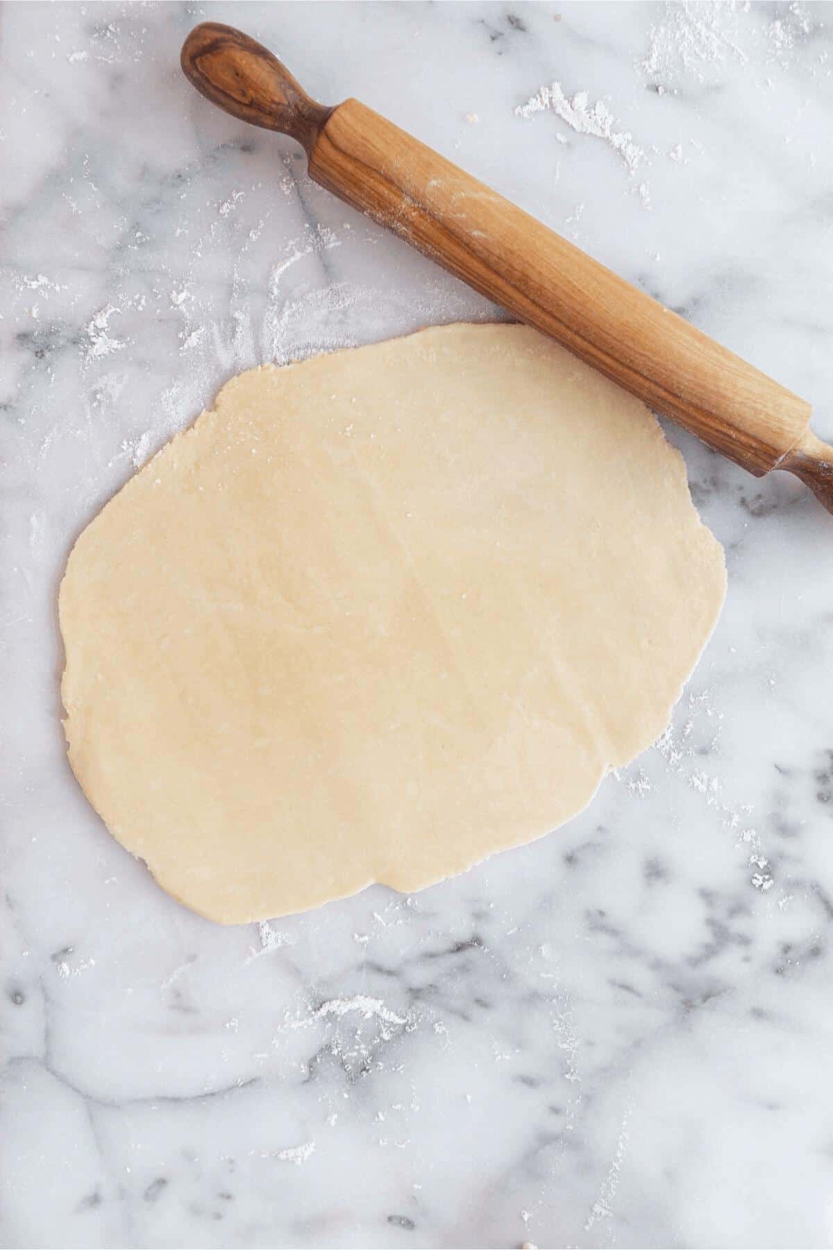 pie crust rolled out on a marble surface and rolling pin