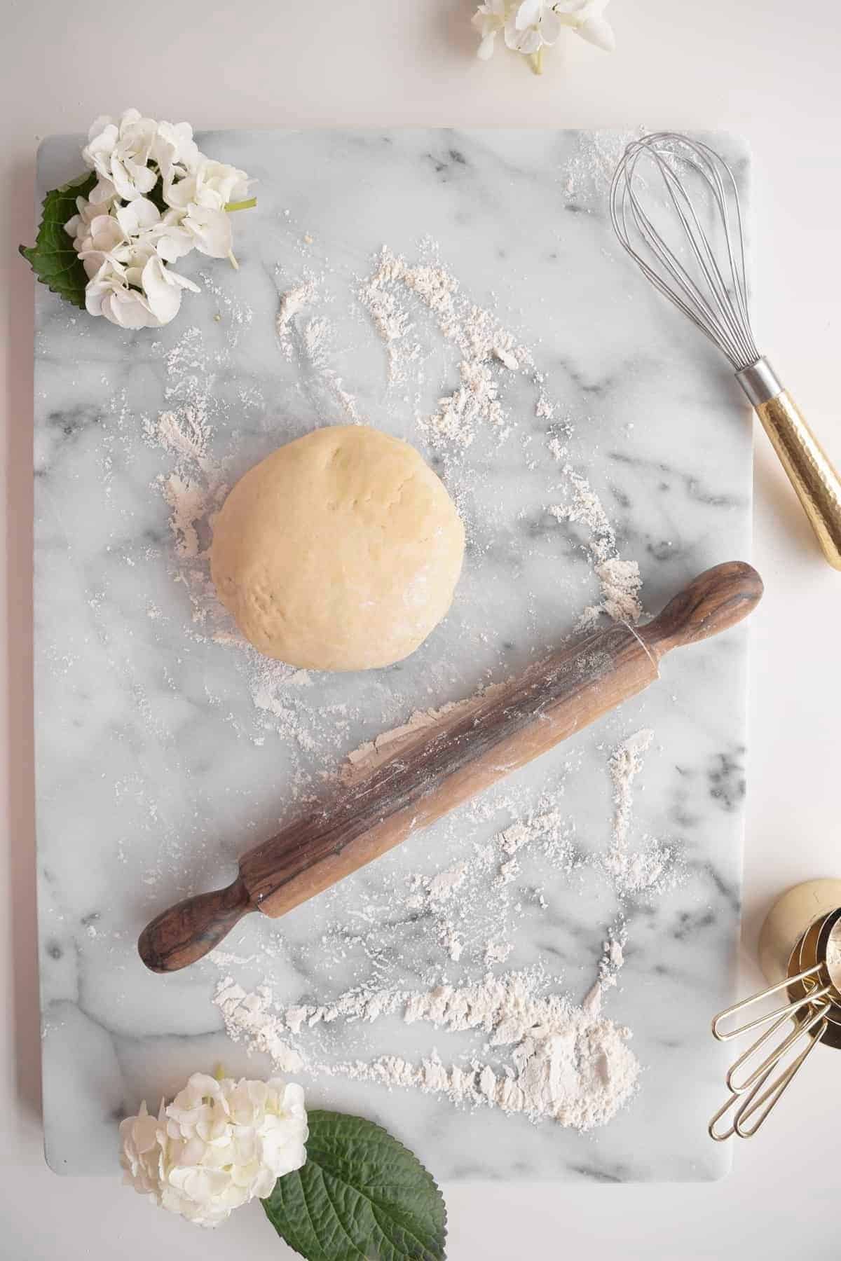 pie dough on a marble surface with flour and rolling pin