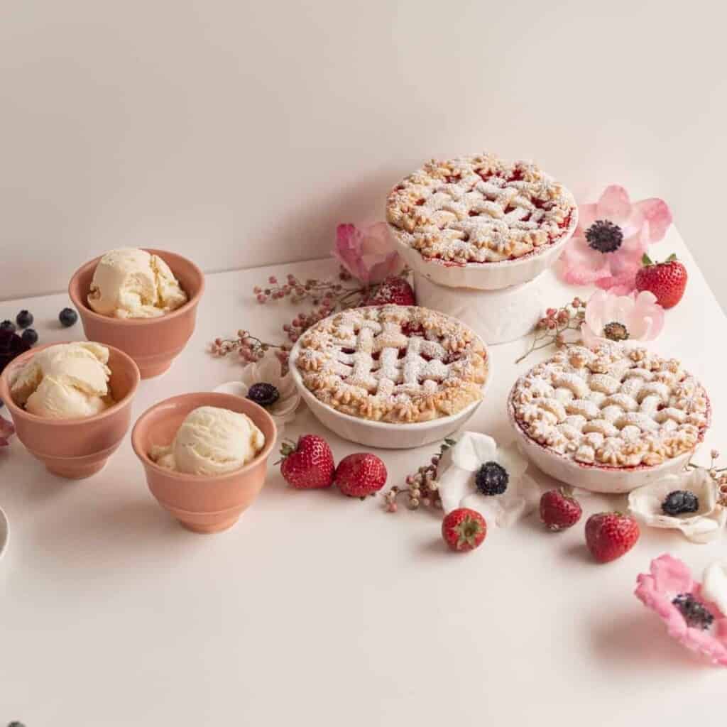 small pies with ice cream with berries and flowers on a white table