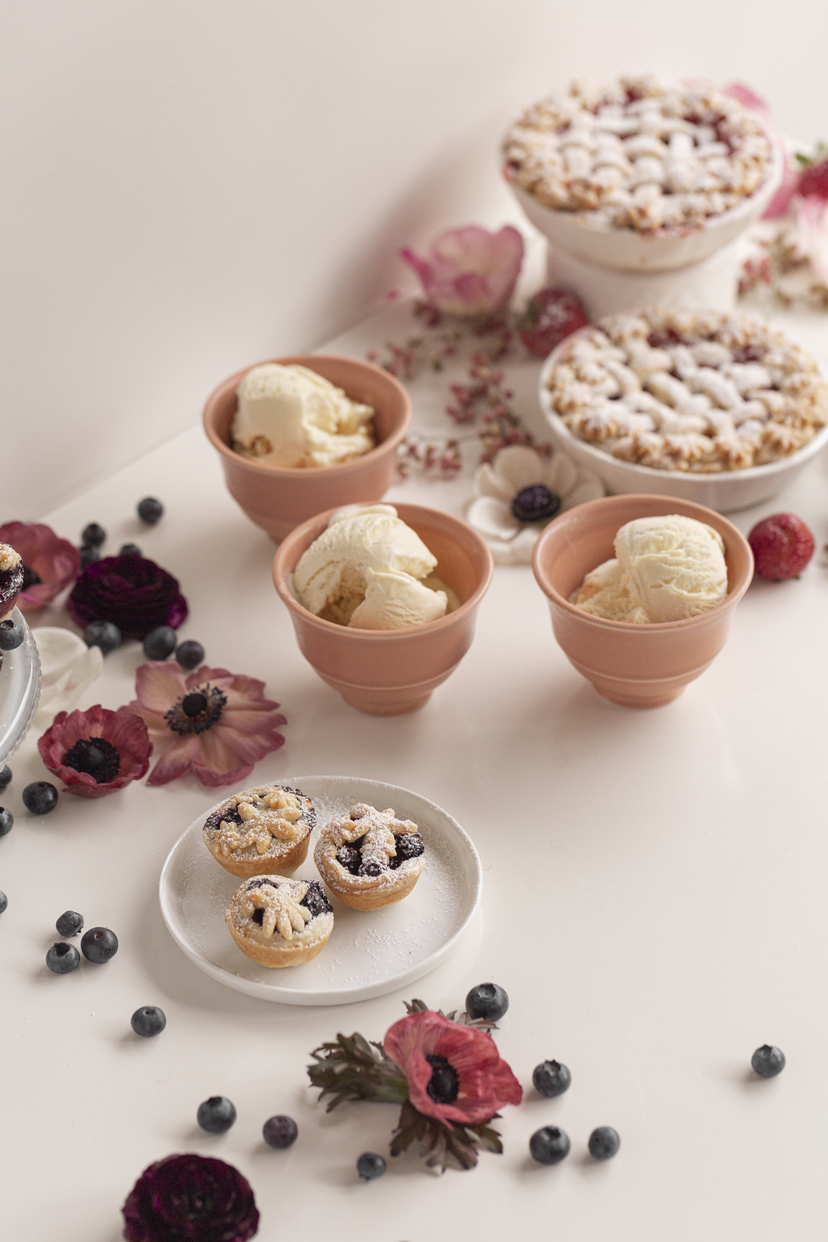 small pies with ice cream with berries and flowers on a white table