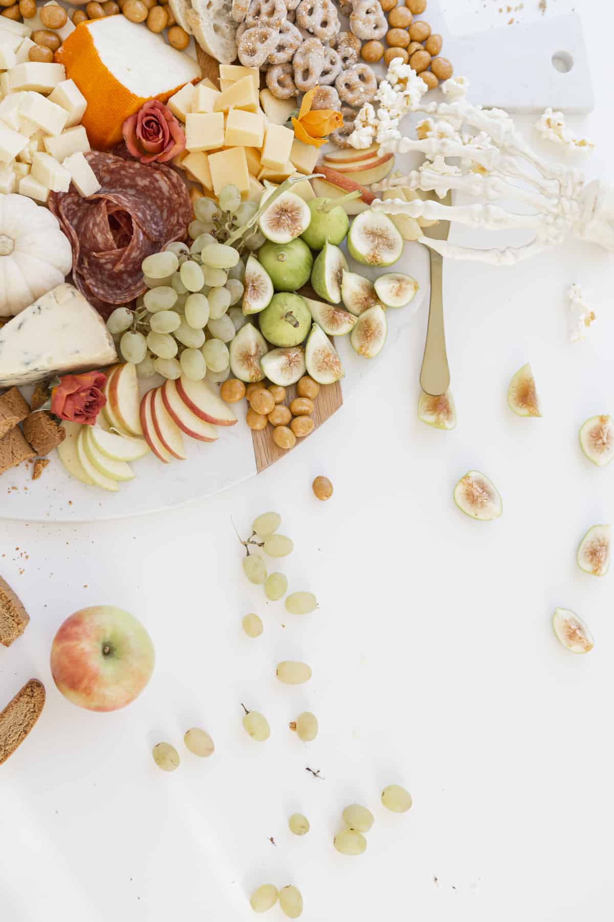 fruits and cheese and salami rose on a board with a skeleton hand