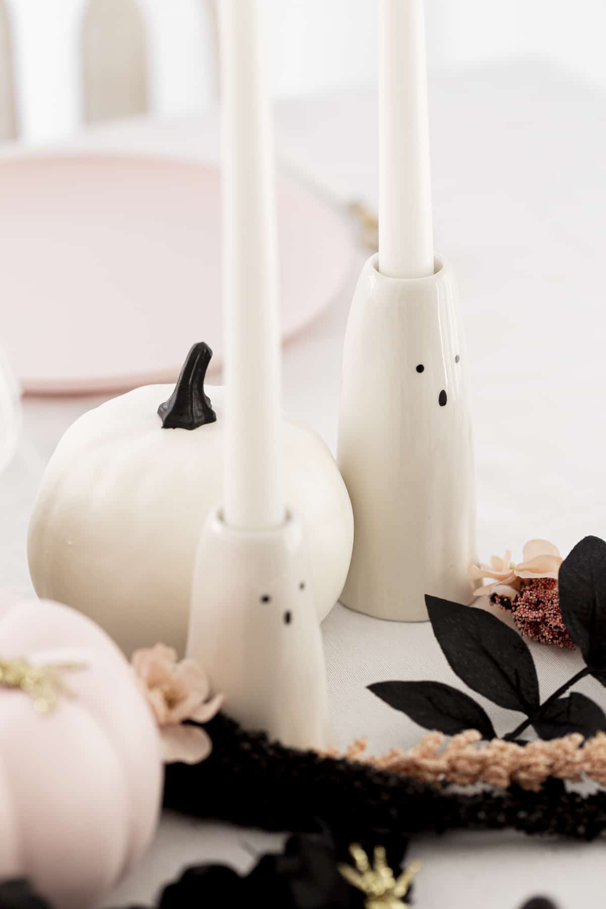 ghost candlesticks with pumpkins and faux flowers on a table