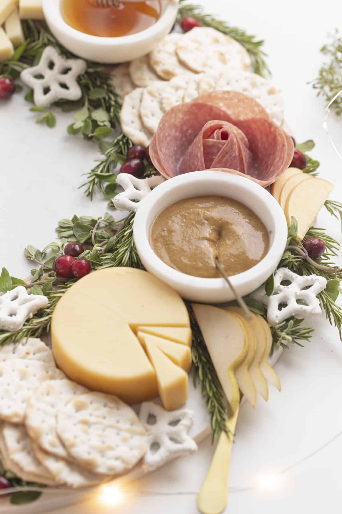 mustard in a bowl next to sliced cheese and salami rose on a charcuterie wreath