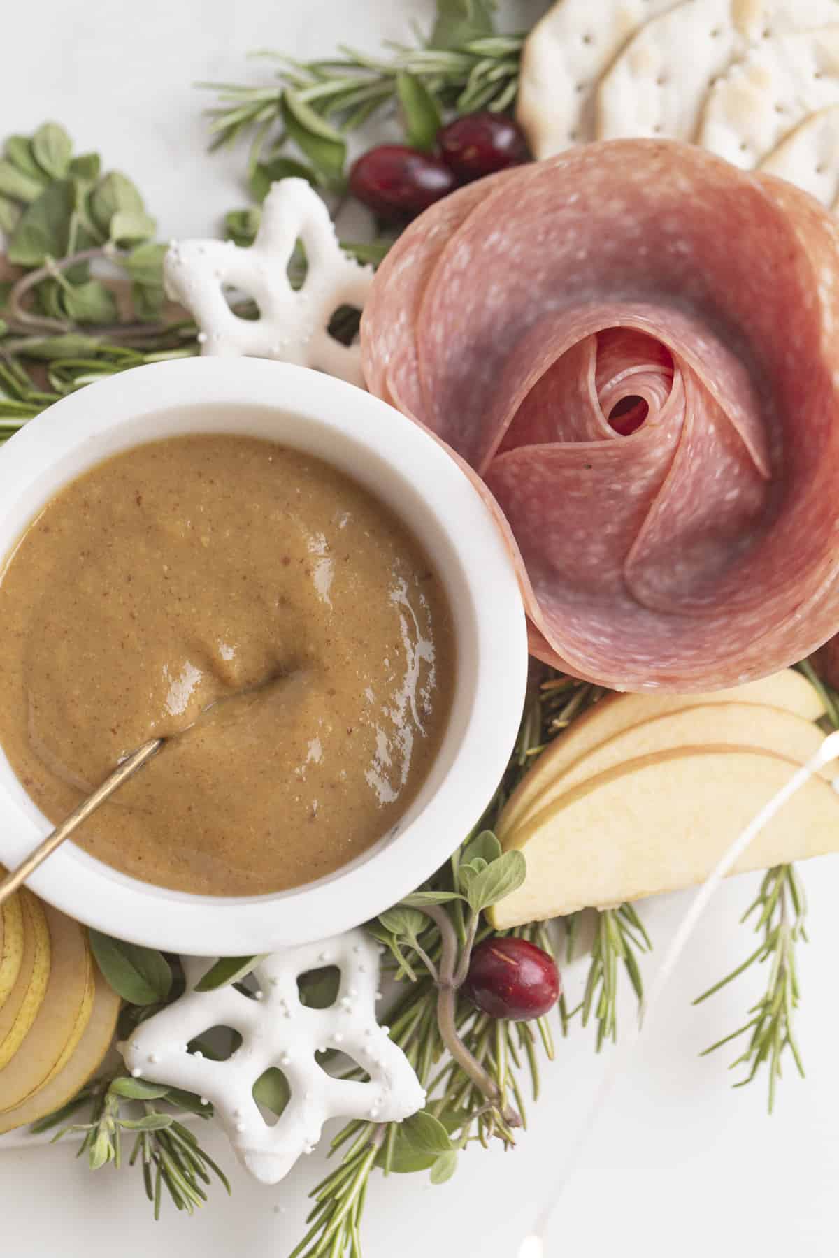 mustard in a bowl next to sliced cheese and salami rose on a charcuterie wreath