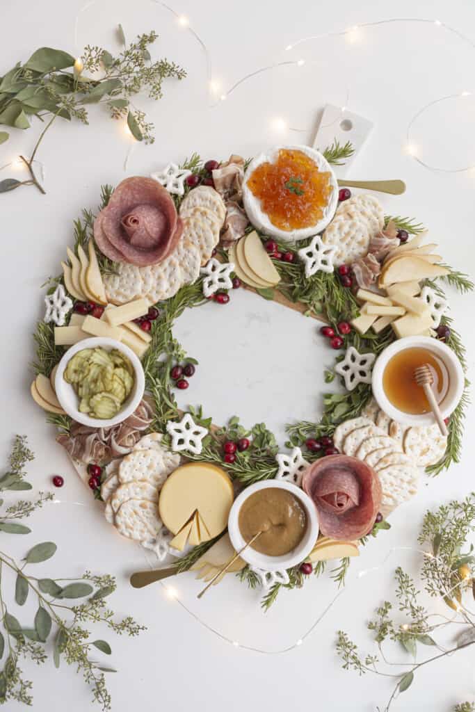 large cutting board with cheese, herbs, and appetizers in a circle