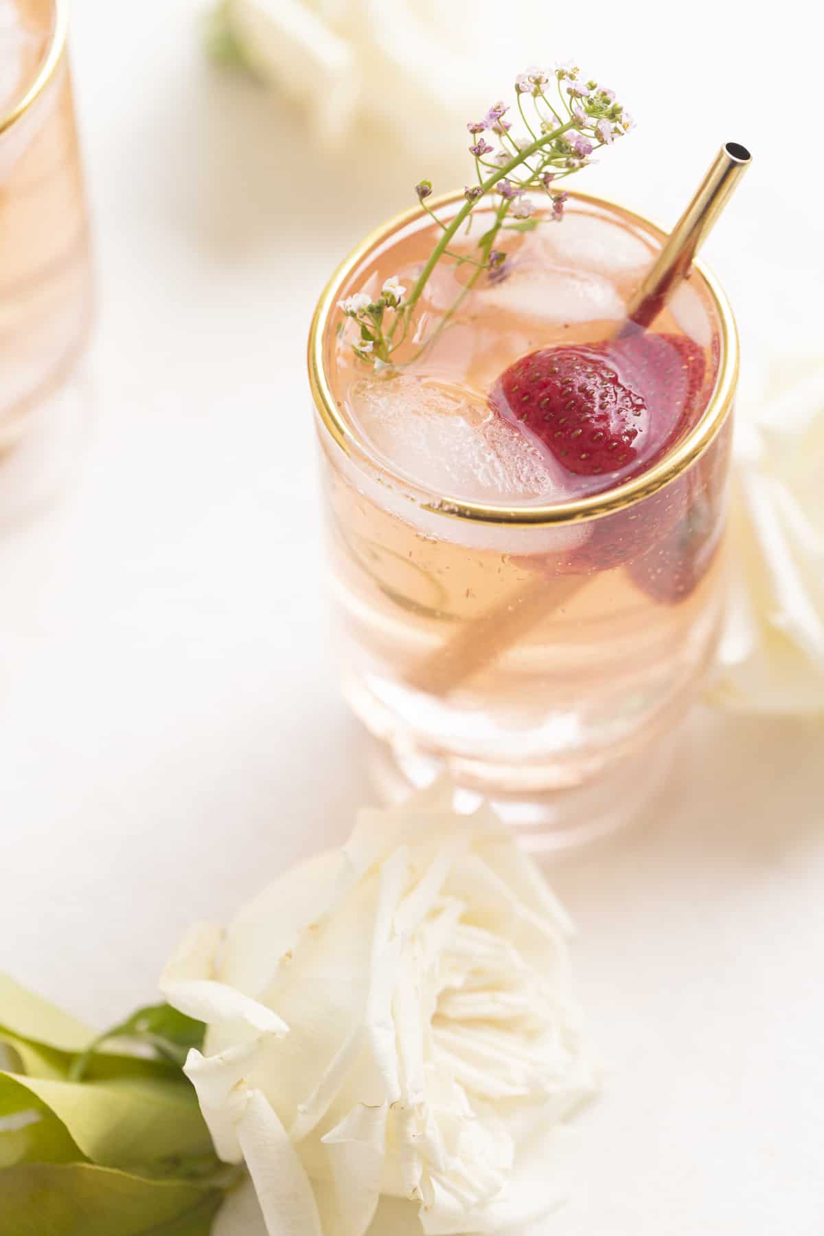 drink in a glass with gold rim, gold straw, strawberry, and purple edible flower