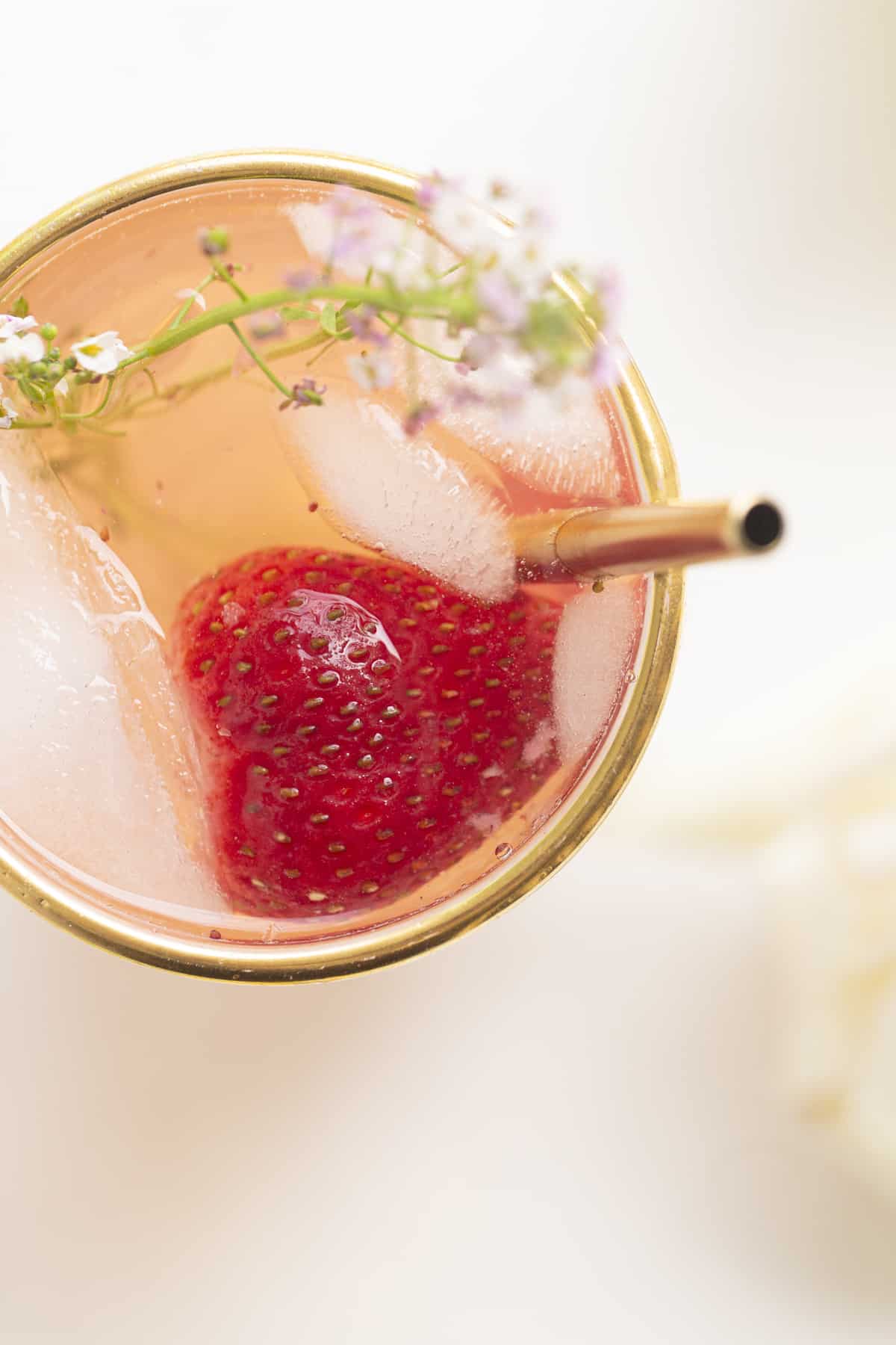 drink in a glass with gold rim, gold straw, strawberry, and purple edible flower