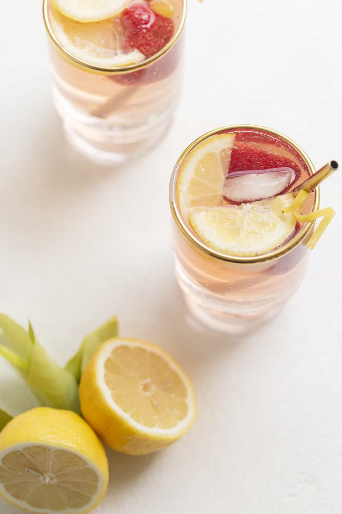 drink in a glass with a gold rim and lemons and strawberry on top
