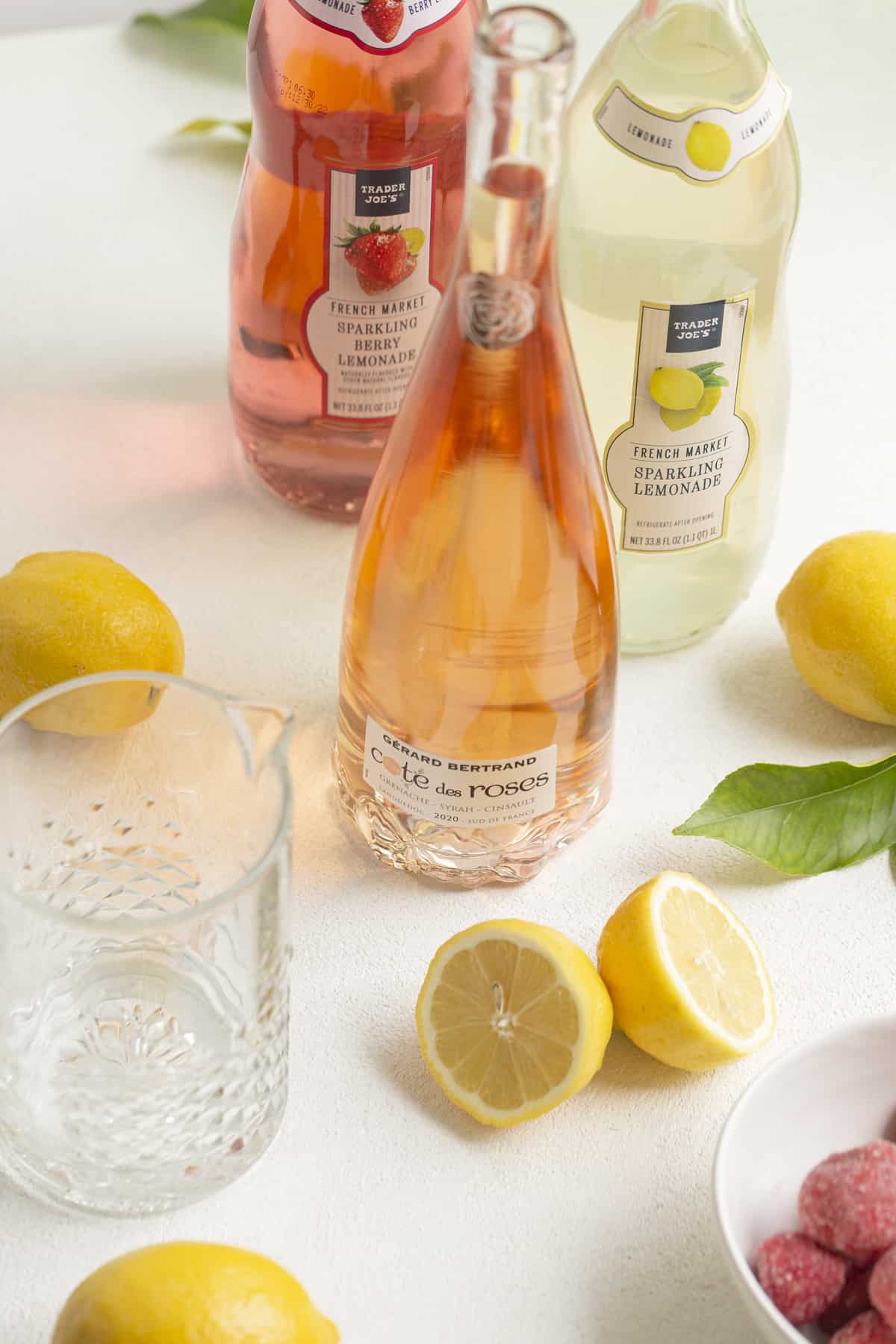 three bottles with lemons and a glass pitcher on a white surface