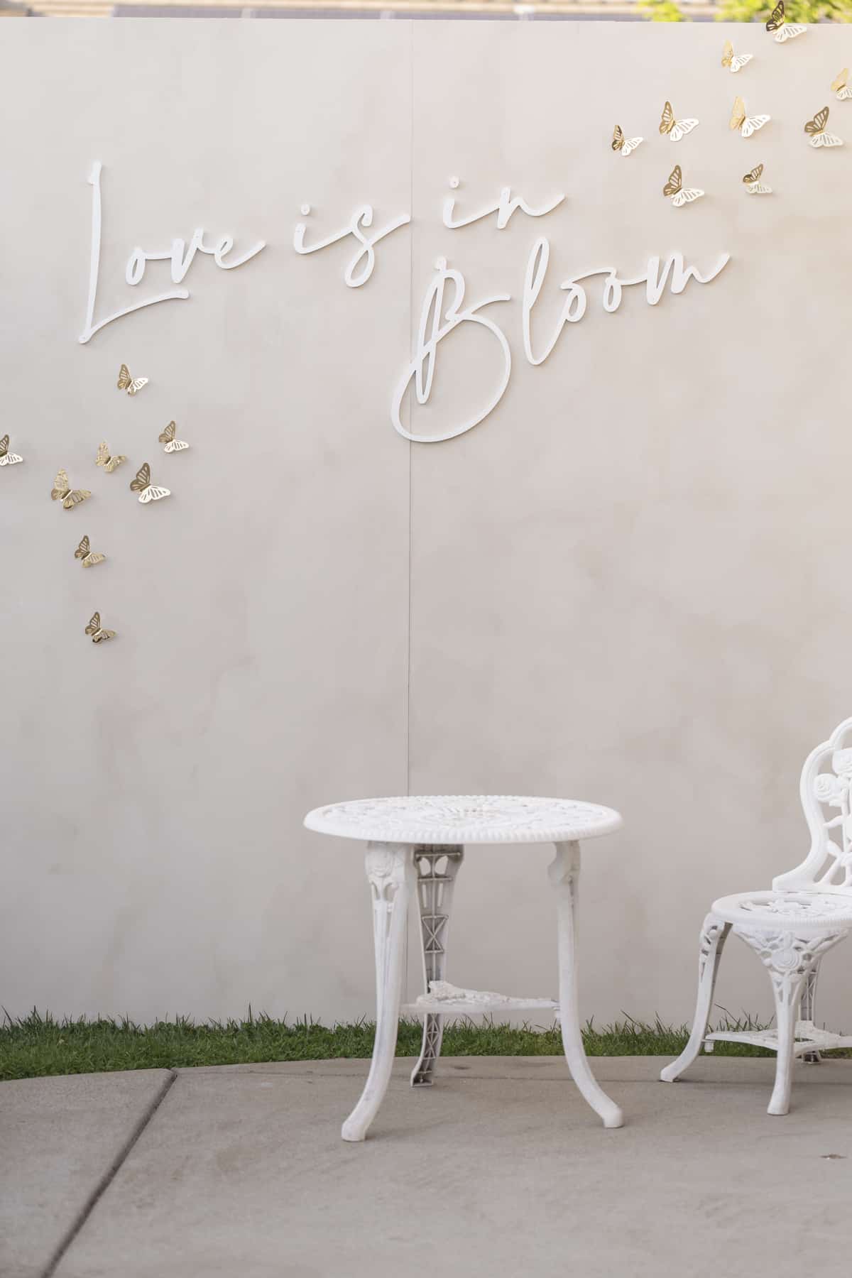 limestone backdrop with white cursive letters spelling "love is in bloom" with gold butterflies