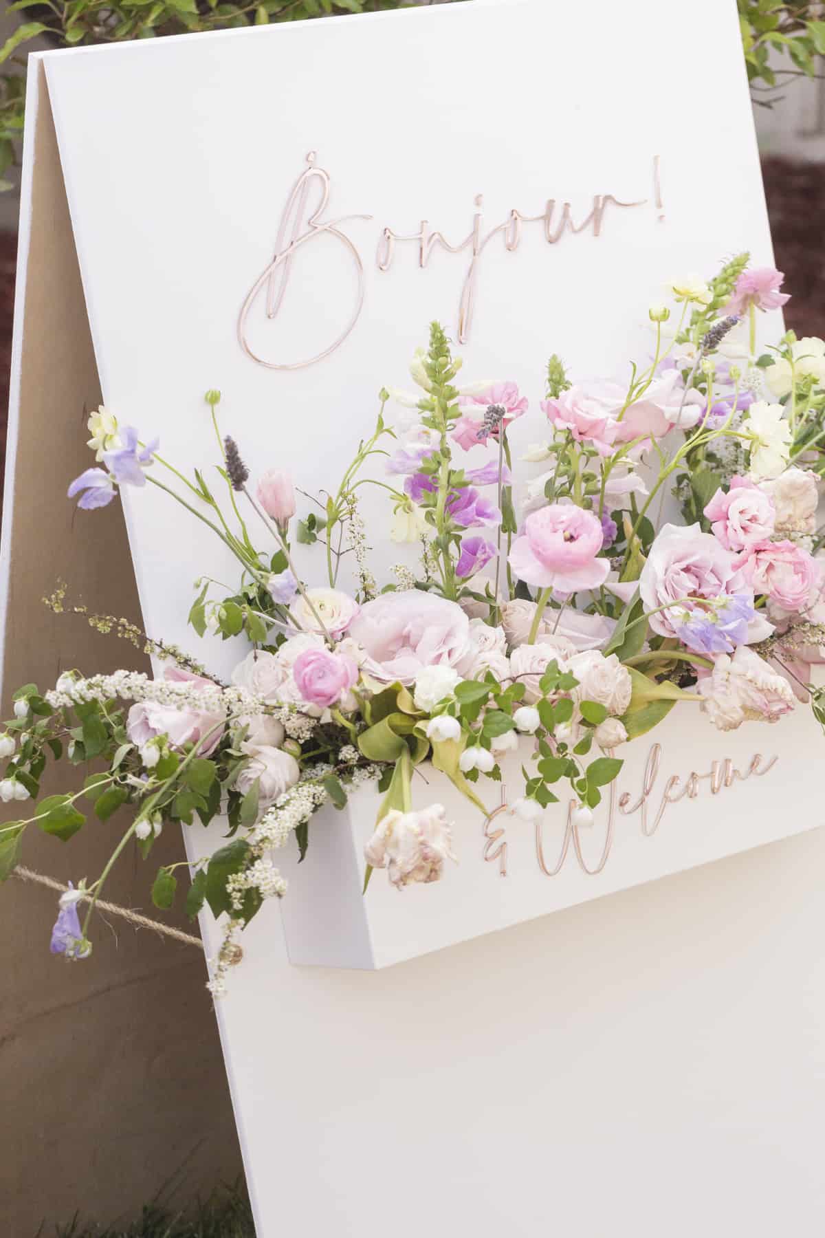 sandwich board sign reading bonjour with pink and purple flowers